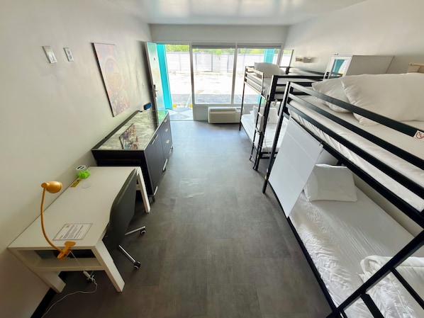 Habitación de hotel con literas, un escritorio con lámpara, un aparador y ventana con vista al exterior.