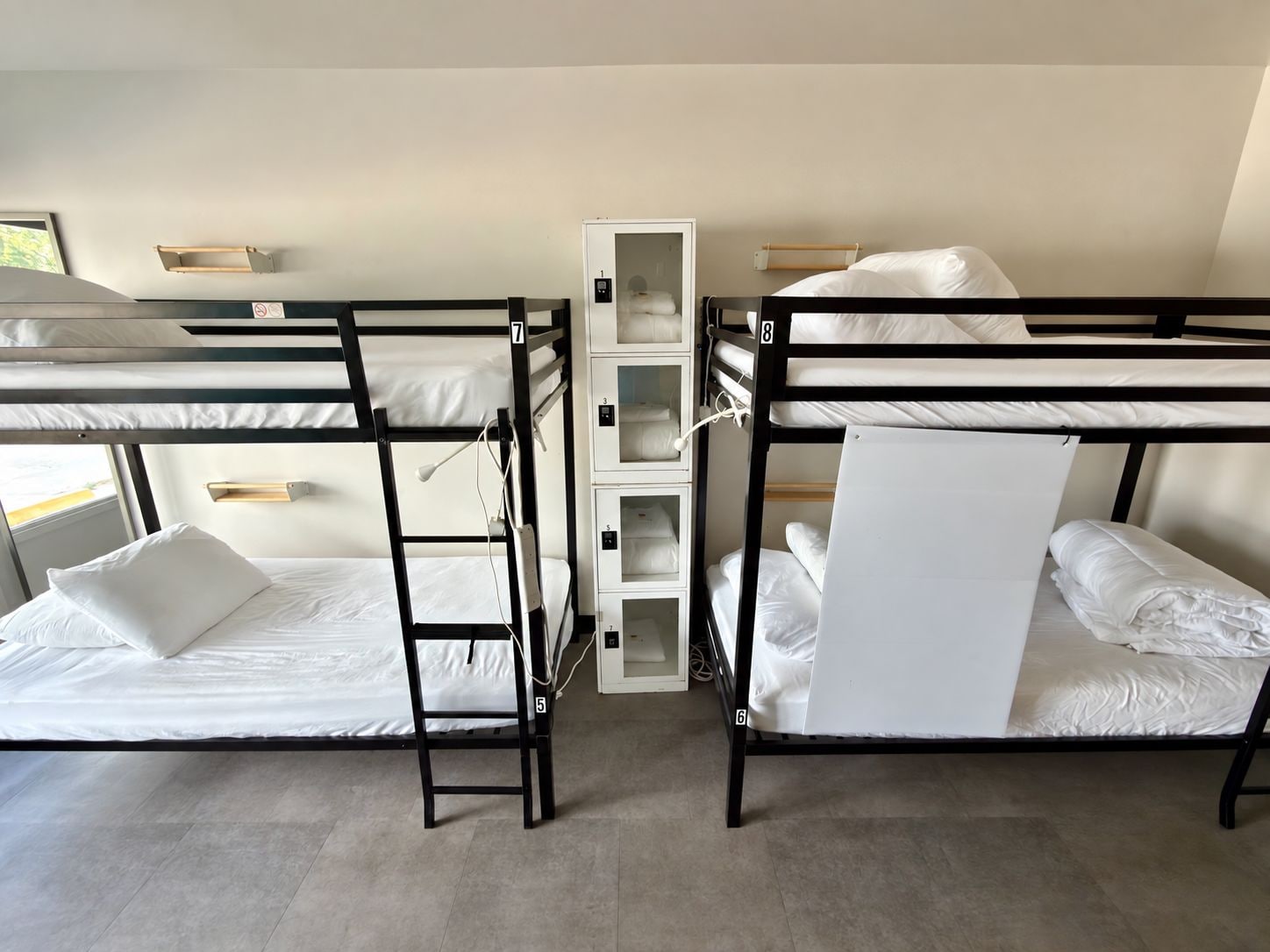 A bunk bed room with two beds, a storage unit, and a window.