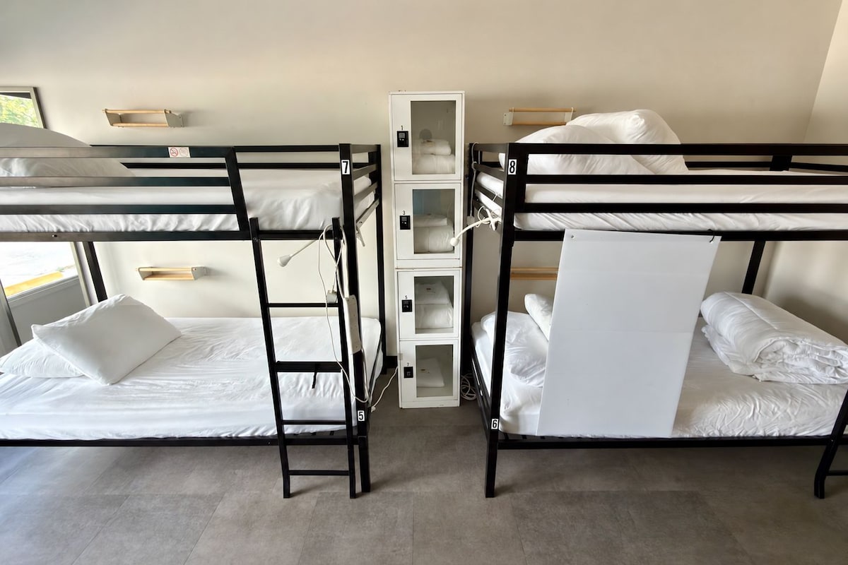 Habitació amb lliteres, dos llits, un moble d'emmagatzematge i una finestra.