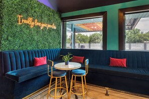 A modern interior with a dark blue sofa, two matching bar stools, a small round table, and a neon sign on the wall. - HOST/EL Boutique Shared Rooms  (Houston)