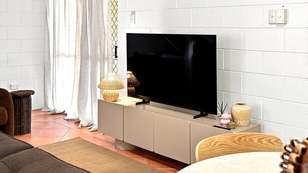En moderne stue med et fladskærms TV på et hvidt skab, en fletlampe og en vase på pejsen.