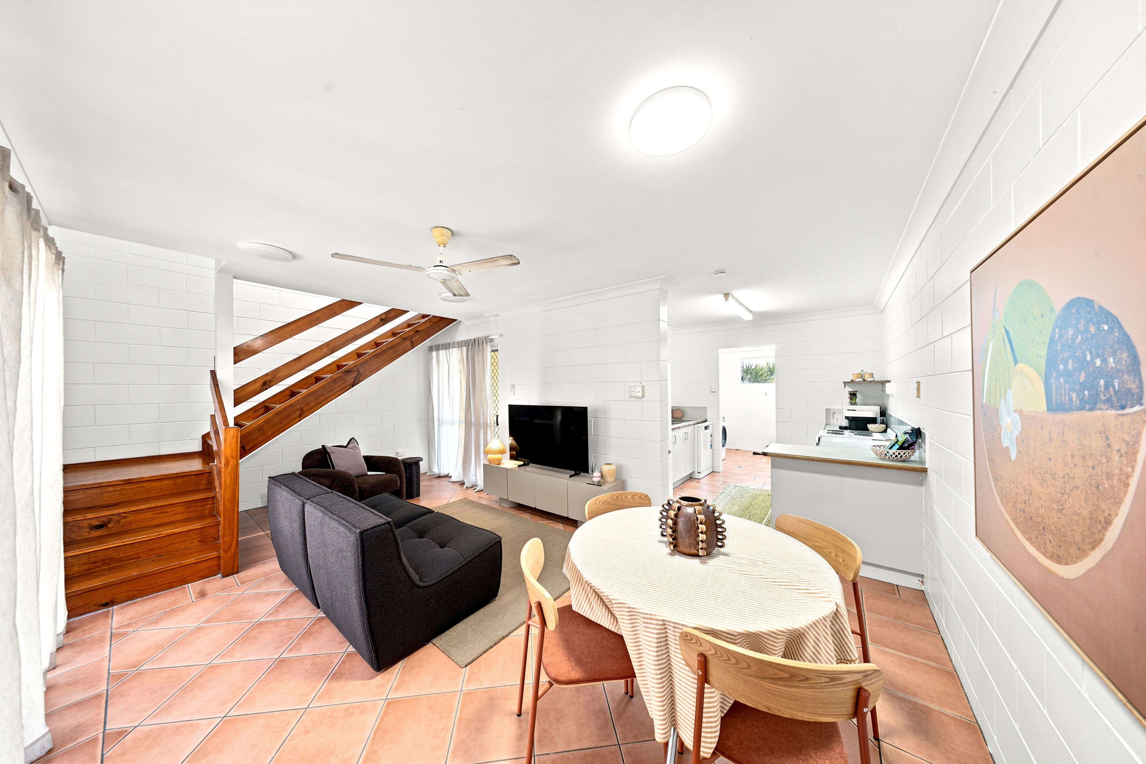 A modern living space with a staircase, a sofa, a dining table, and a kitchen area.