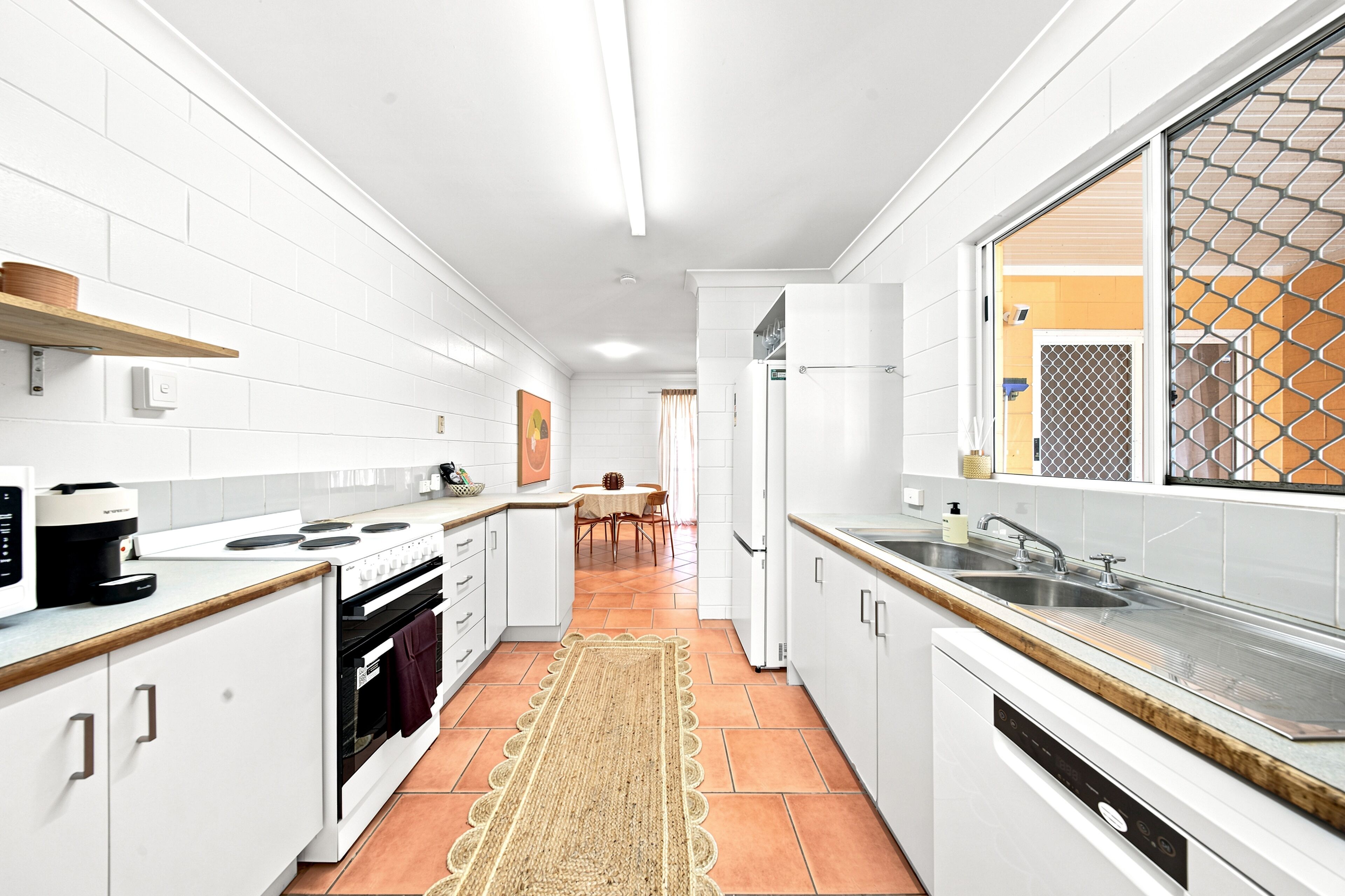 Eine moderne Küche mit weißen Schränken, einem Herd, einem Backofen und einem großen Fenster mit einem Metallgitter.