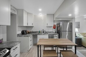 A modern kitchen with white cabinets, a stainless steel refrigerator, a wooden dining table, and a built-in oven. - Backyard Breeze: Modern 1BR with Walk-In Shower Near BNA (Nashville)