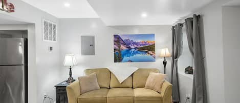 A living room with a sofa, a coffee table, a painting, a lamp, and a refrigerator.