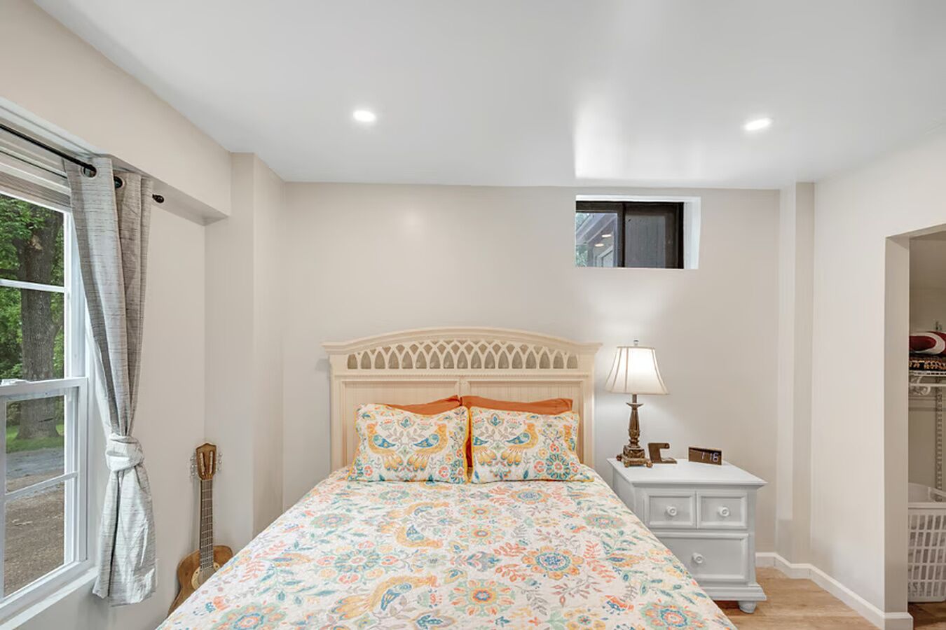Une chambre à coucher avec un lit, une table de chevet, une lampe, une guitare et une fenêtre avec des rideaux.