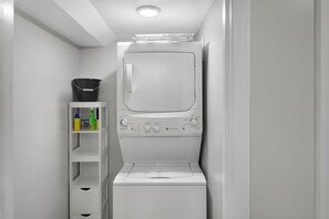 Ett kompakt tvättrum med en inbyggd tvättmaskin och torktumlare, en hylla med rengöringsmedel och en vit dörr.