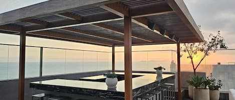 A rooftop terrace with a bar area, seating, and potted plants.