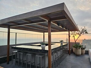 Terraza en la azotea con área de bar, asientos y plantas en macetas.