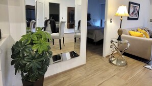 Ein modernes Wohnzimmer mit einem großen Spiegel, einer Zimmerpflanze, einer Couch, einer Lampe und einem Bett im Hintergrund.