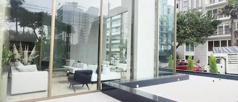 Un intérieur moderne avec de grandes fenêtres en verre, un coin salon avec des canapés blancs et une vue sur le paysage urbain.