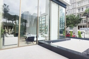 A modern interior with large glass windows, a seating area with white sofas, and a view of the cityscape. - Luxury Barranco Apartm. Rooftop Pool Gym (Lima)