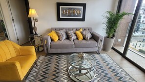 A modern living room with a sofa, a yellow armchair, a glass coffee table, and a large potted plant. - Luxury Barranco Apartm. Rooftop Pool Gym (Lima)