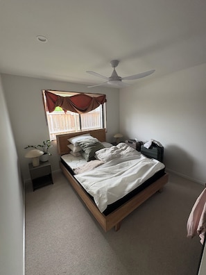 A bedroom with a bed, a ceiling fan, a window with curtains, a bedside lamp, and a small table with a plant. - Coastal short term rental (Golden Beach)