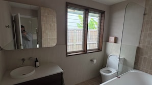 Ein Badezimmer mit Badewanne, Toilette, Waschbecken und einem Fenster mit Jalousien.