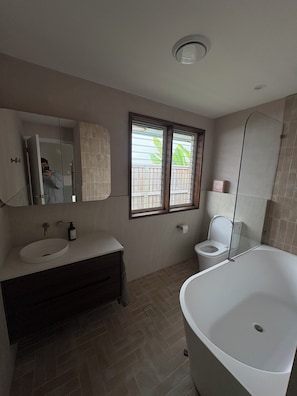 A bathroom with a bathtub, toilet, sink, and a window with blinds. - Coastal short term rental (Golden Beach)