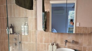 Ein Badezimmer mit einer Duschkabine aus Glas, einem weißen Waschbecken und einem hölzernen Waschtisch.