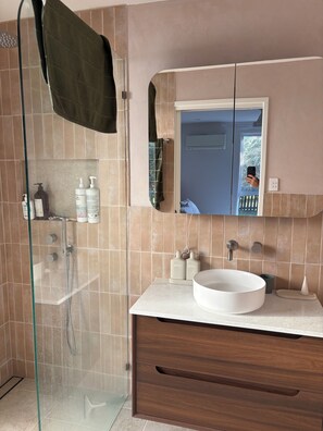 A bathroom with a glass-enclosed shower, a white sink, and a wooden vanity. - Coastal short term rental (Golden Beach)