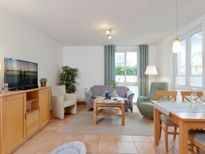 A living room with a television, seating area, dining table, and a view of the outdoors. - Apartment Building Linquenda 08 (Heringsdorf)