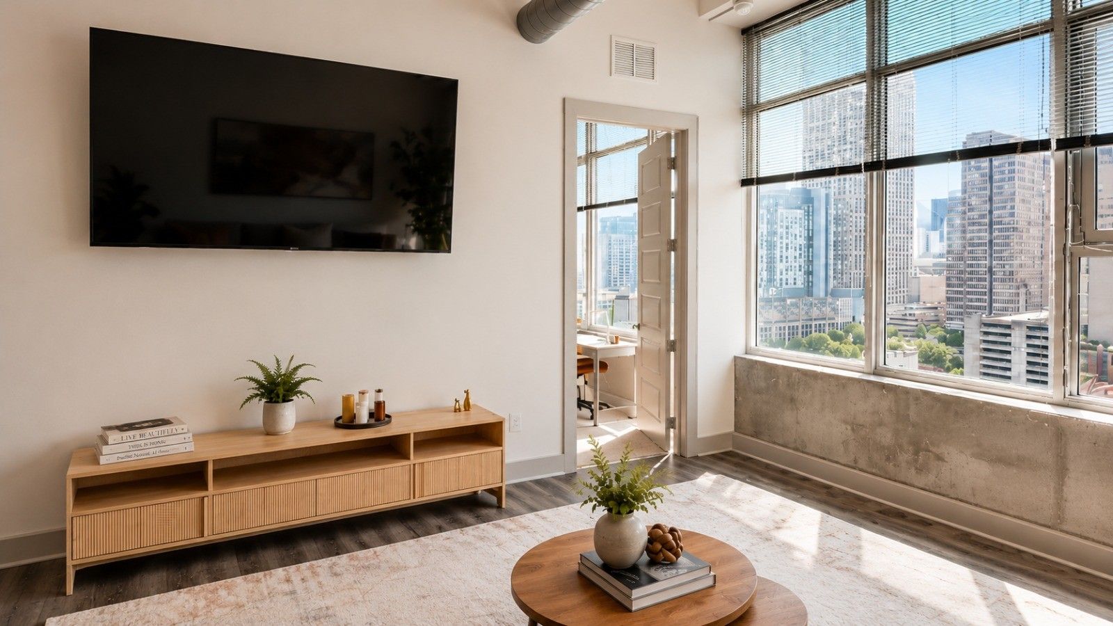 Een moderne woonkamer met een grote televisie, een houten console en een stadszicht door grote ramen.