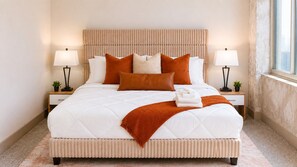 A neatly made bed with a headboard, two bedside tables with lamps, and a window with a view. - Stylish King Suite • Walk to Downtown (Atlanta)