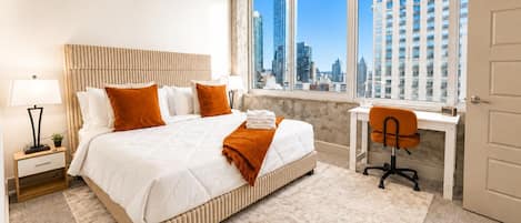A modern hotel room with a large bed, a desk, and a view of the city skyline.