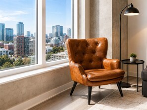 A leather armchair with a tufted backrest and black legs, positioned next to a window with a view of a cityscape. - Stylish King Suite • Walk to Downtown (Atlanta)