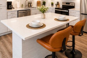 A kitchen with a central island, two bar stools, and a coffee maker.