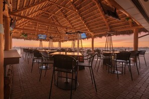 An outdoor dining area with thatched roof, tables, and chairs, overlooking a scenic view. - King Studio -waterfront views from private balcony with boat dock. (Sarasota)