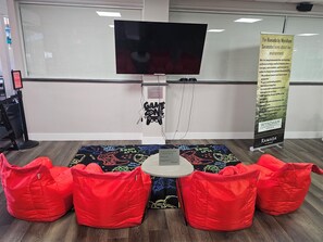 Una habitación con una televisión de pantalla plana montada en la pared, un cartel sobre políticas ambientales y sillones de hidrantes rojos dispuestos alrededor de una pequeña mesa.