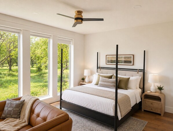 A bedroom with a four-poster bed, large windows, a ceiling fan, and a view of greenery outside.
