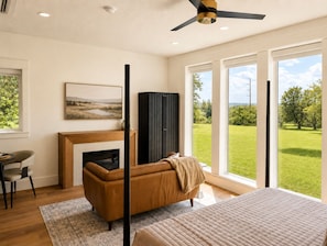 Un dormitorio moderno con chimenea, un sofá, una cama y un gran ventanal con vistas a un paisaje verde.