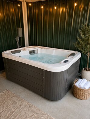 A hot tub in a spa area with a dark wooden floor, a potted plant, and a basket of towels.