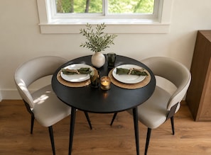 A round dining table with two chairs, a vase with green foliage, two plates with wrapped items, and two glasses.