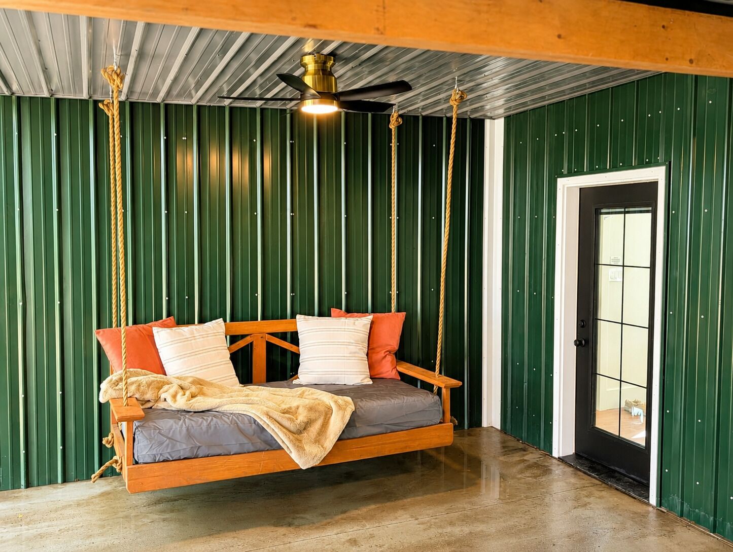 A room with a swing bed, a ceiling fan, and a door with a window.