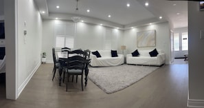 Ein modernes Wohnzimmer mit Essbereich, weißen Möbeln und einem großen Gemälde an der Wand.