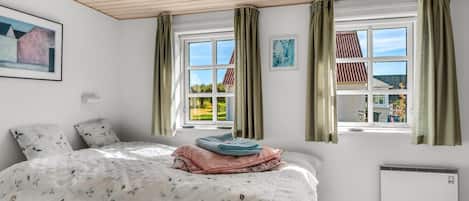 A bedroom with a bed, two windows, a radiator, and a painting on the wall.