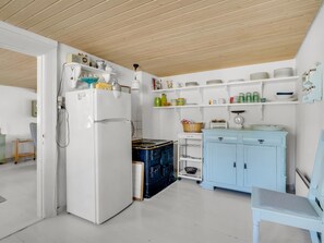 A compact kitchen with a white refrigerator, a blue stove, and white shelves with various kitchen items. - "Safir" - 1.7km from the sea by Interhome (Snedsted)