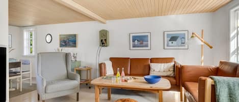 Een ruime woonkamer met een hoge plafond, een zithoek, een salontafel en een televisie.