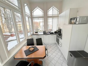 Eine moderne Küche mit großen Fenstern, einem Esstisch mit Stühlen und einem Kühlschrank.