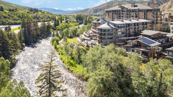 A modern hotel complex with multiple buildings, a river running through the property, and a mountainous backdrop.