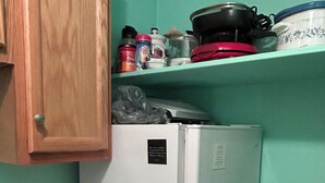 Une cuisine avec un réfrigérateur blanc, des placards en bois, un plan de travail et une étagère contenant divers ustensiles de cuisine.