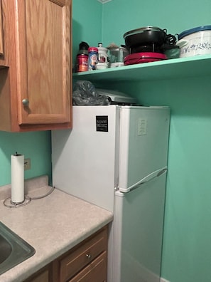A kitchen with a white refrigerator, wooden cabinets, a countertop, and a shelf with various kitchen items.