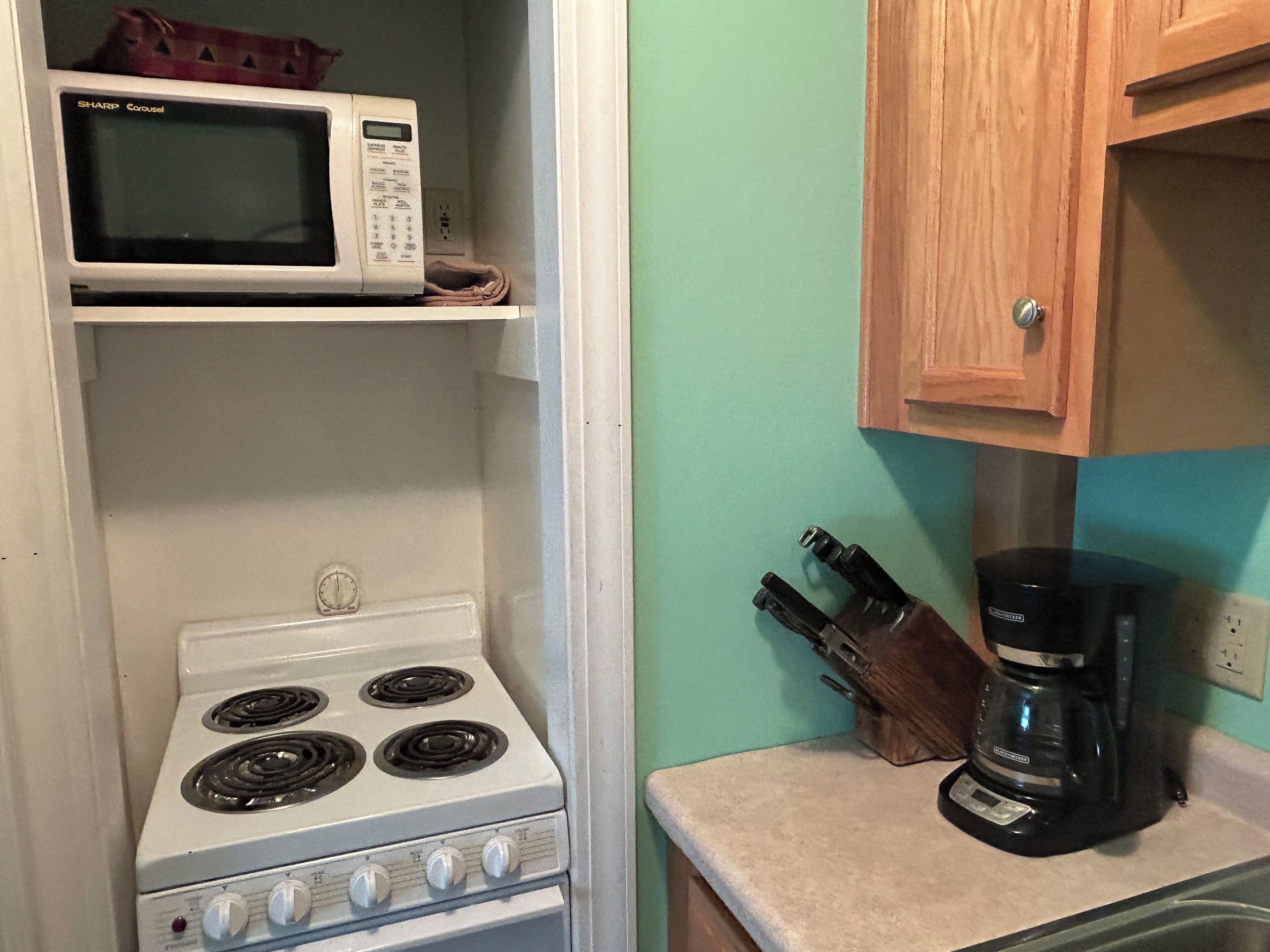 A kitchen with a white stove, a microwave on a shelf, and a coffee maker on the counter.
