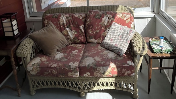 Une pièce chaleureuse avec un canapé en osier, un tapis à motifs et une vue sur une forêt, visible à travers de grandes fenêtres.