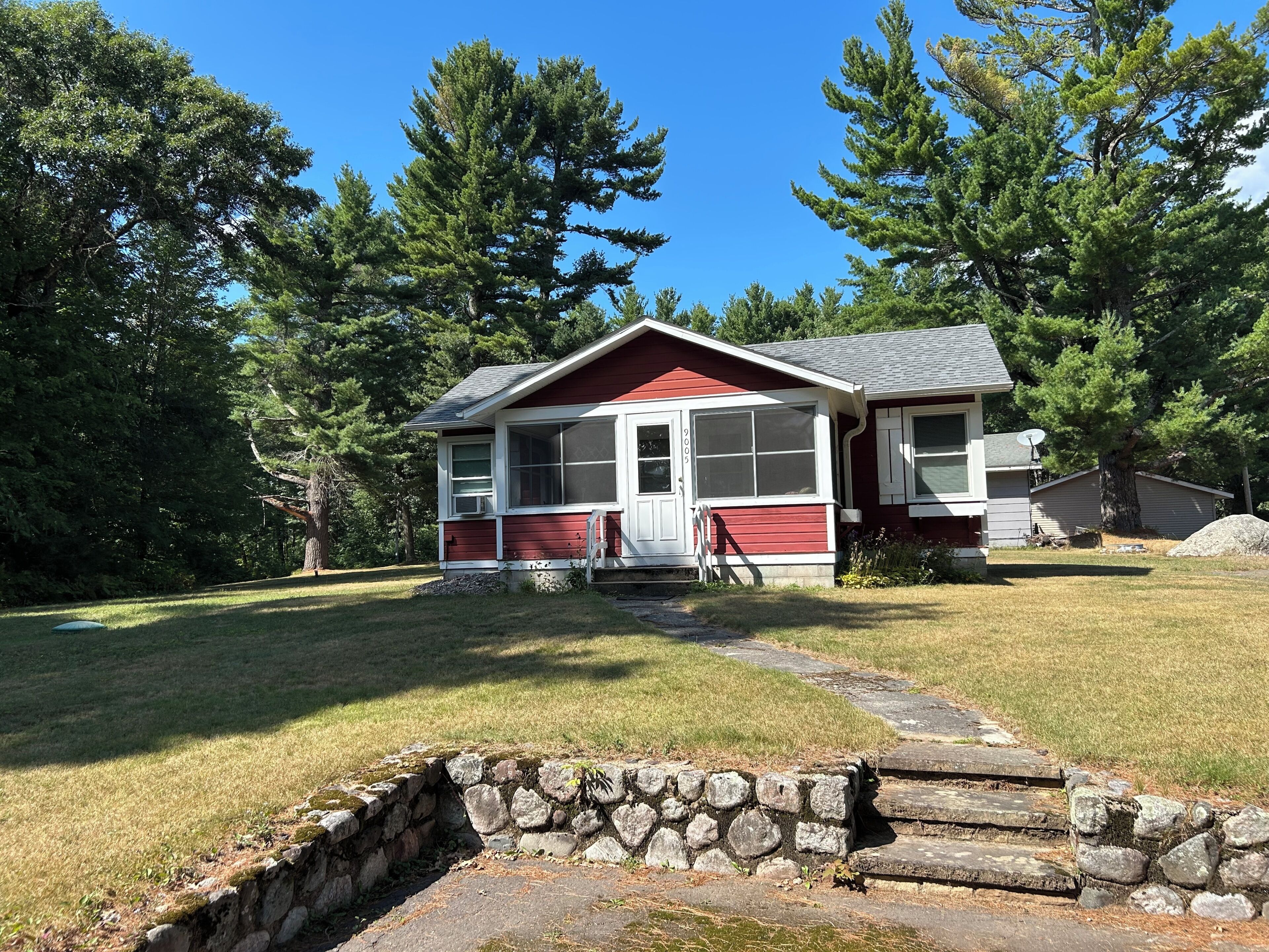 A single-story house with a red and white exterior, a front porch, and a stone retaining wall.