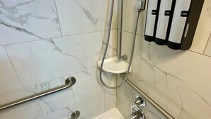 Ein Badezimmer mit Badewanne, Haltegriffen, einer Handbrause und einem wandmontierten Seifenspender.
