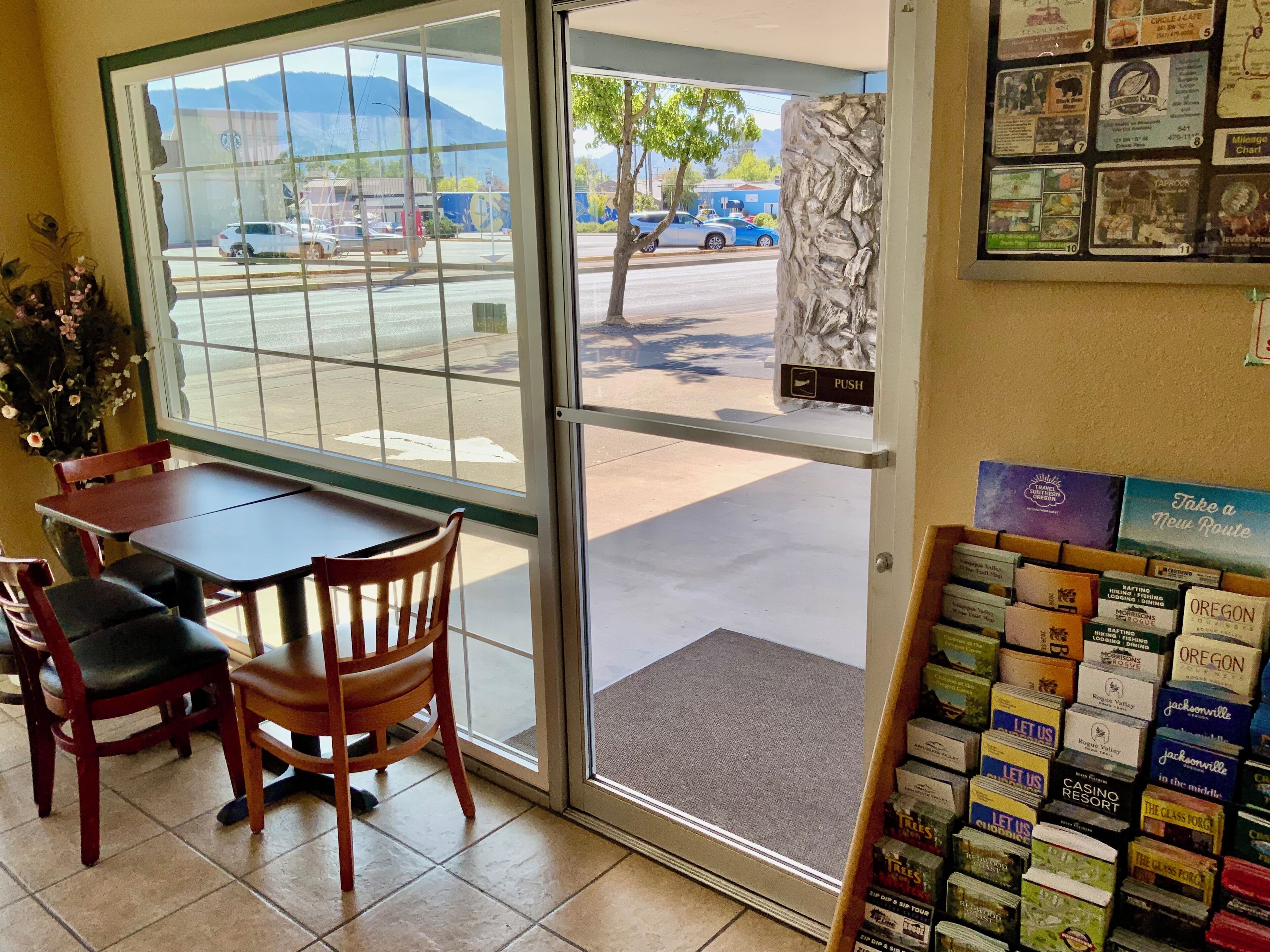 A restaurant interior with a table and chairs, a display of travel brochures, and a view of the street outside.
