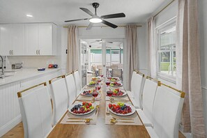 A dining area with a long table set for a meal, white chairs, and a ceiling fan. - Splash & Relax! Games•WiFi•BBQ•Fire Pit•Boat•Lake (Royal Palm Beach)