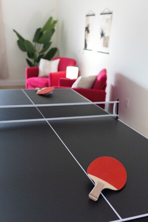 A ping pong table with a paddle, a red chair, and a plant in a room with white walls.